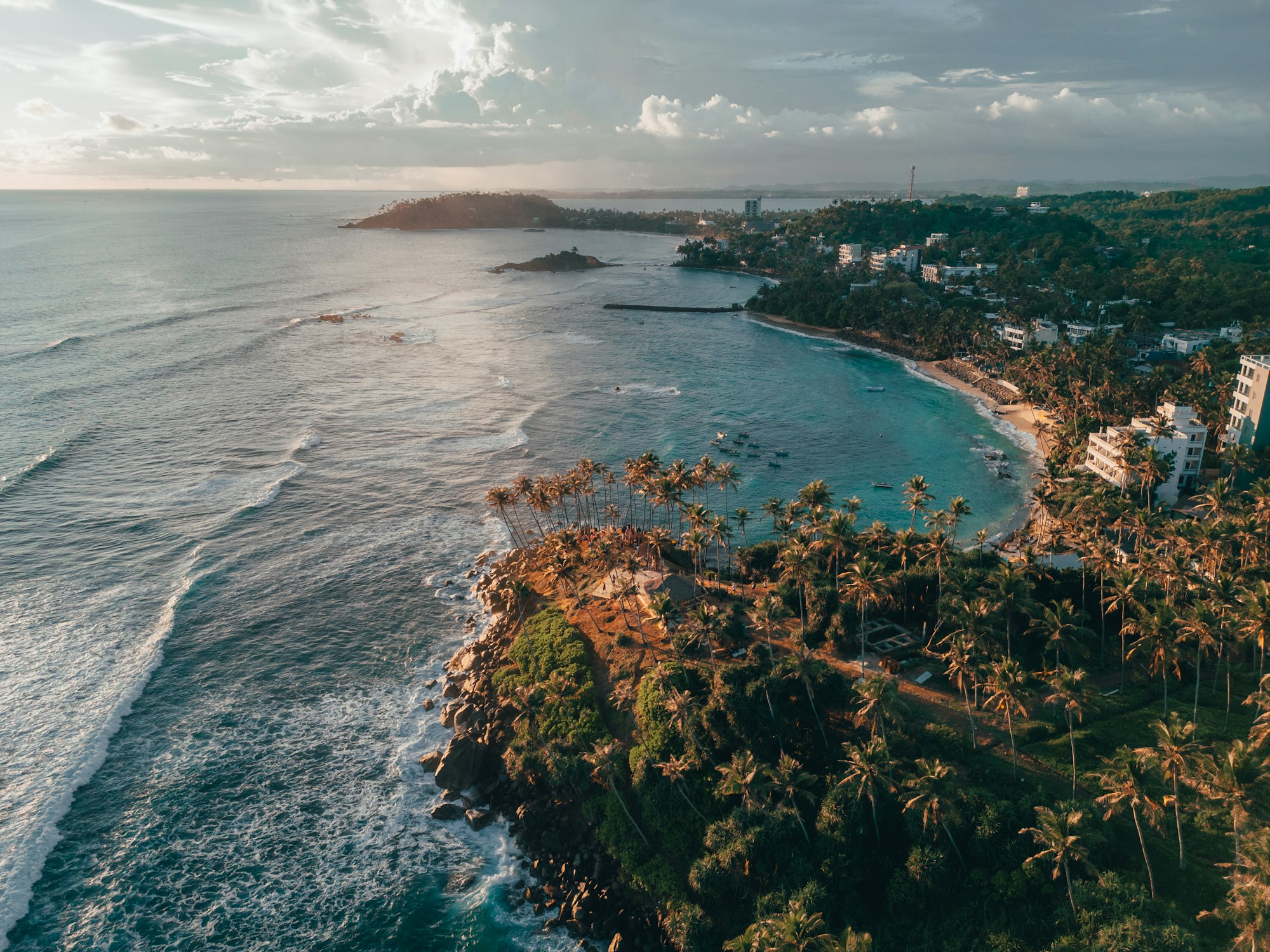 Aerial view of a palm-fringed bay on the Sri Lankan south coast, with surf breaking around a green headland